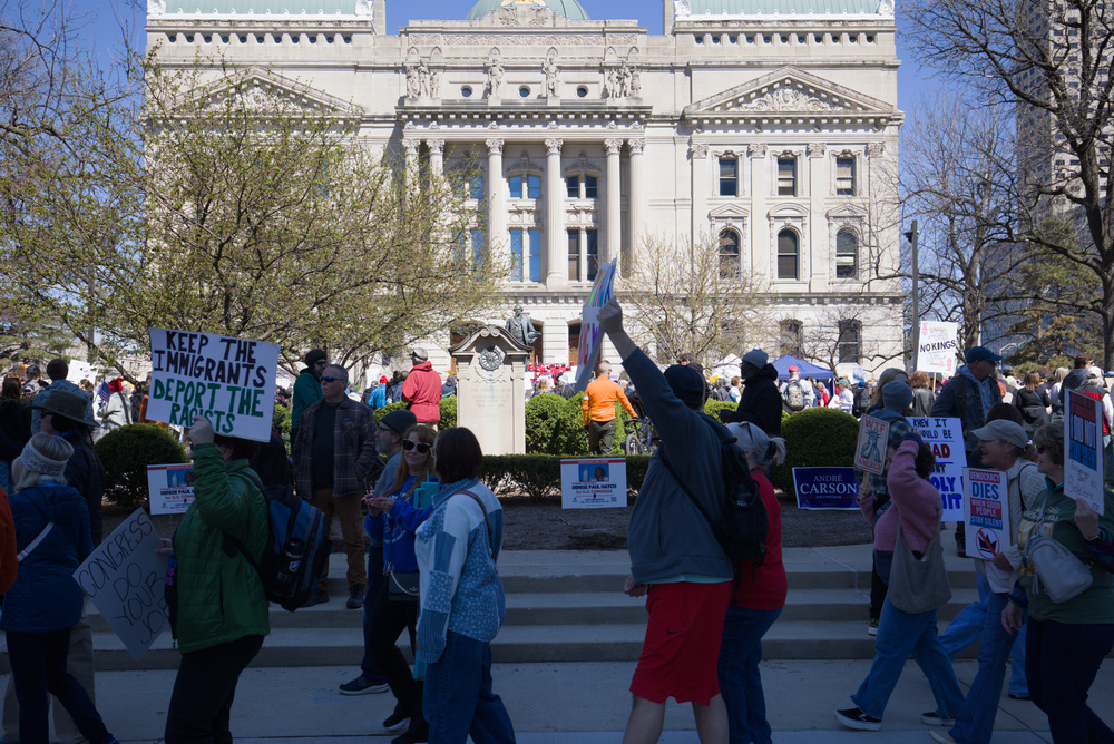 a crowd of people holding signs marches past the statehouse