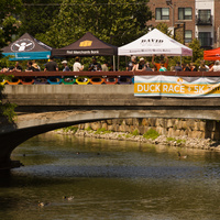A Duck Race banner hangs from the bridge, which has several tents and scores of people on it.